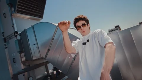 Man dancing on rooftop with industrial equipment in side view, energetic urban Stock Footage 345152955