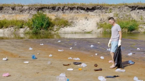 Man is dancing, singing acollects plastic trash on banks of polluted river Stock Footage 125054563
