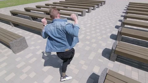 Man dancing street modern dance in a park between rows of benches. Slow motion Stock Footage 132659912
