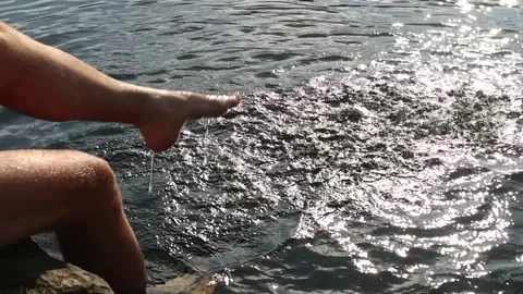 Man dangles his legs in the water of lake. Splashing water Video stock 249055022