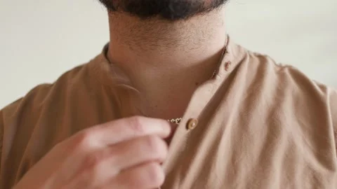 Man with a dark beard, wearing a watch and a necklace with 'queer,' unbuttoning Stock Footage 296722510