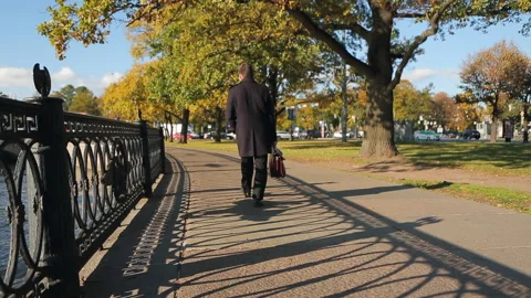 A man in a dark coat and with a briefcase walks along the autumn embankment. Stock Footage 220266072