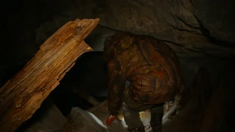 A man in the dark with a flashlight climbs into a dark cave. Stock Footage 86076284