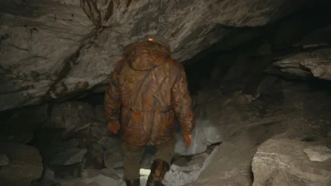 A man in the dark with a flashlight walking along a dark cave Stock Footage 86077509