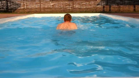 Man in dark shorts jumps into a pool and swims off camera Stock Footage 99935142