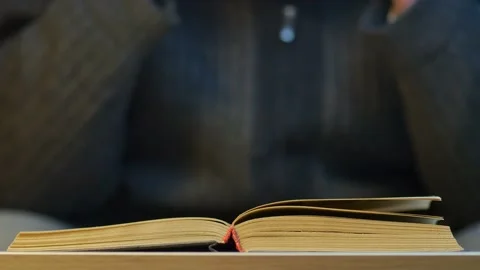 Man in a dark sweater puts on glasses and reads an old book Stock Footage 237497461