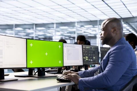 Man in data center updating systems on green screen PC to protect servers Stock Photos