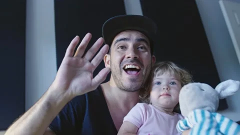 Man with daughter in lap waving to camera Stock Footage 143292617