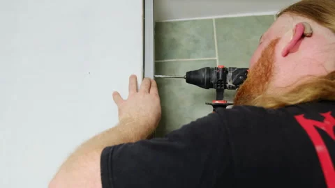 Man with deaf-aid makes hole in plank with electric drill Stock Footage 304404898