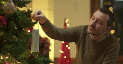 Man decorates christmas tree with face mask Stock Footage 143853174