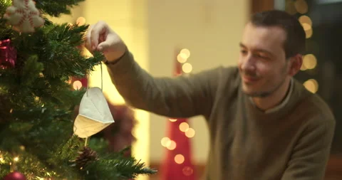 Man decorates christmas tree with face mask Stock Footage 143854087