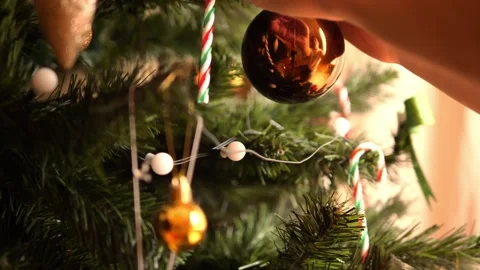 Man decorates christmas tree with shiny brown bauble, Christmas tree glows with  Vidéo 293347324