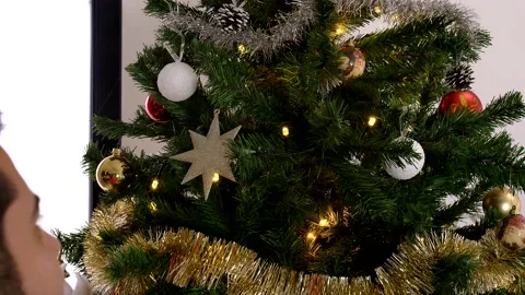 Man decorating Christmas tree with red ball. He is wearing a red sweater. Stock Footage 140847512