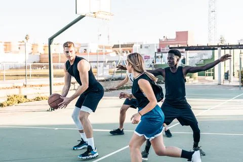 Man defending a ball while playing basketball with friends in an outdoor court Stock Photos