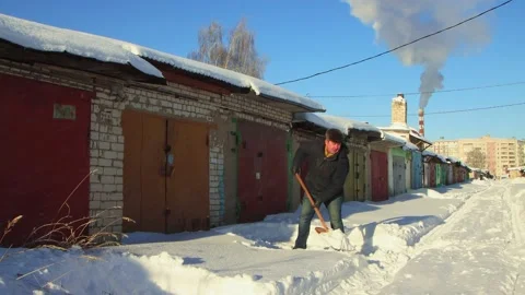 A man deftly clears the passage to the garage from snow with a wooden shovel. Stock Footage 225836544