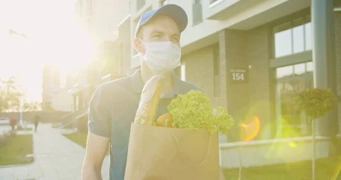 Man delivery worker wearing blue cap and medical mask walking the street and Stock Footage 129557999
