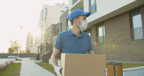 Man delivery worker wearing blue cap and medical mask walking the street and Stock Footage 129559486