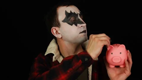 Man in demon makeup putting a coin in piggy bank and saving money Video stock 146584680