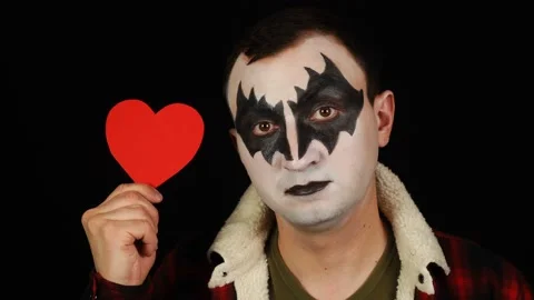 Man in demon makeup raising red heart then showing it at the camera on black Stock Footage 146579695