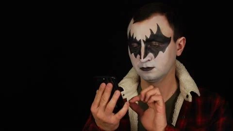 Man in demon makeup using his smartphone on black background Stock Footage 146584419