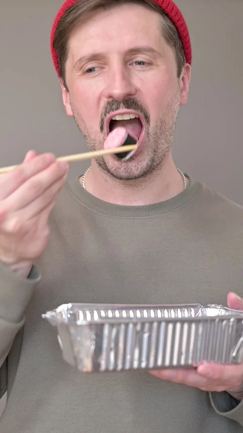 A man demonstrates the use of chopsticks while eating from a metallic container. Видео 337556157