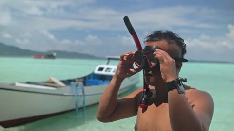 Man demonstrating how to use a snorkel and swimming goggles against a clear blue Stock Footage 341959582