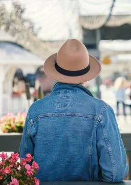 A man in a denim jacket and a hat stands with his back and looks at the busy Stock Photos