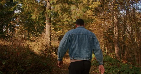 Man in denim jacket walking through a forest in autumn. Exploration and solitude 스톡 동영상 265006072