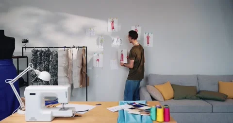 Man designer standing in atelier, looking at sketches hanging on wall Vídeo Stock 220146940