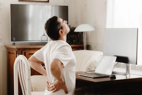 Man at a desk with a computer with back pain Stockfoto's