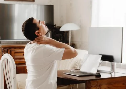 A man at a desk with a computer sips his neck Stockfoto's