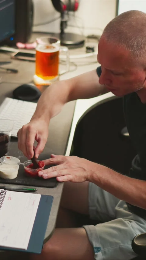 Man at desk dipping jerky into sauces with computer monitors and glass of amber Stock Footage 345980690