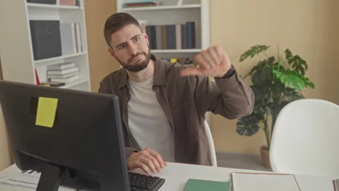 Man at desktop computer typing on keyboard while giving a thumbs down with .. Stock Footage 347815384