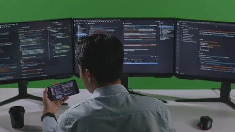 Man Developer Working With Mobile Phone While Write Code With Multiple Computer Stock Footage 249632598