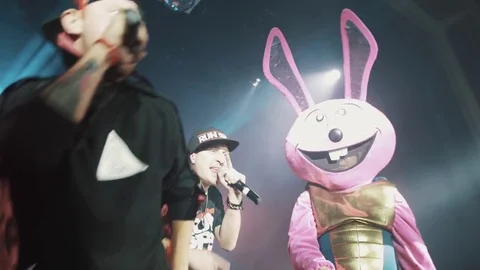 Man in devil costume rapping from scene with pink rabbit mascot flashing lights Stock Footage 71813384