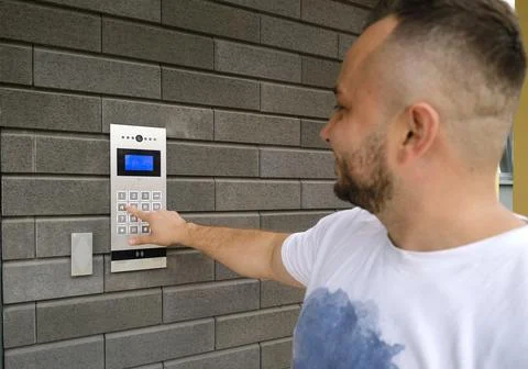 Man dials the code for the video intercom outside building to go home Stock Photos