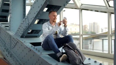 Man dials a message on a smartphone sitting on an iron structure 스톡 동영상 91373313