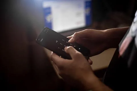 A man dials a number that starts with plus 4 on his smartphone. Dark background. Stock Photos