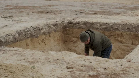Man digging a deep hole in the ground at a construction site during daylight Stock Footage 317083339