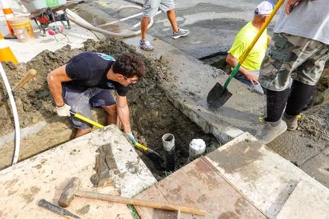 Man digging a hole in a driveway to replace a broken pipe Stock Photos