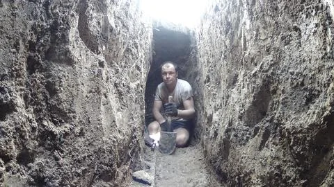 A man is digging a hole. Sits in a deep hole, trench Stock Photos