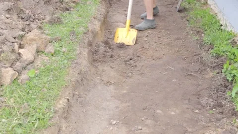 A man digs the ground with a shovel. A worker digs the ground with a shovel. A 库存影片 250938779