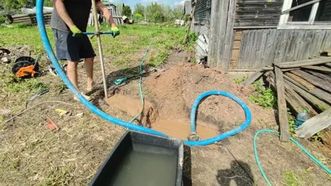 Man digs trench and sets up water pump in rural area on a sunny day for drainage Stock Footage 336158466