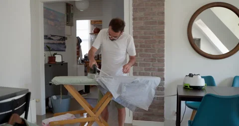 A man diligently irons clothes on a board 库存影片 344311517