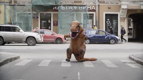Man in dino mascot costume posing at city street crosswalk Stock Footage 84932168