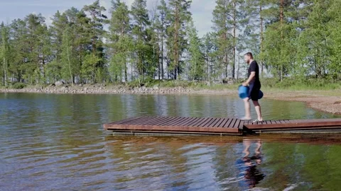 Man dips a bucket into the clean water of Lake Saimaa from a wooden dock. Stock Footage 344903123