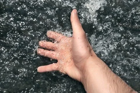 A man dips his hand in a stream of creek. Stock Photos