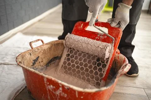 Man dips a paint roller to wipe off the excess paint on the squeegee Stock Photos