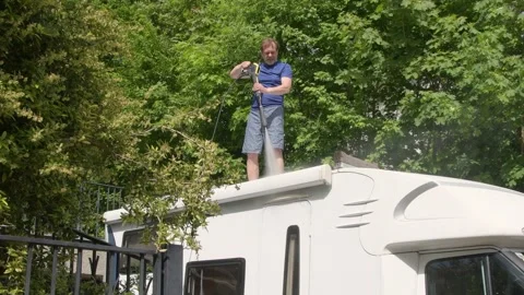 Man directing powerful water spray onto white residential camper, Vidéo 334569387