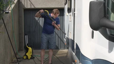Man directing water spray onto white motorhome surface in summer, 库存影片 334569094